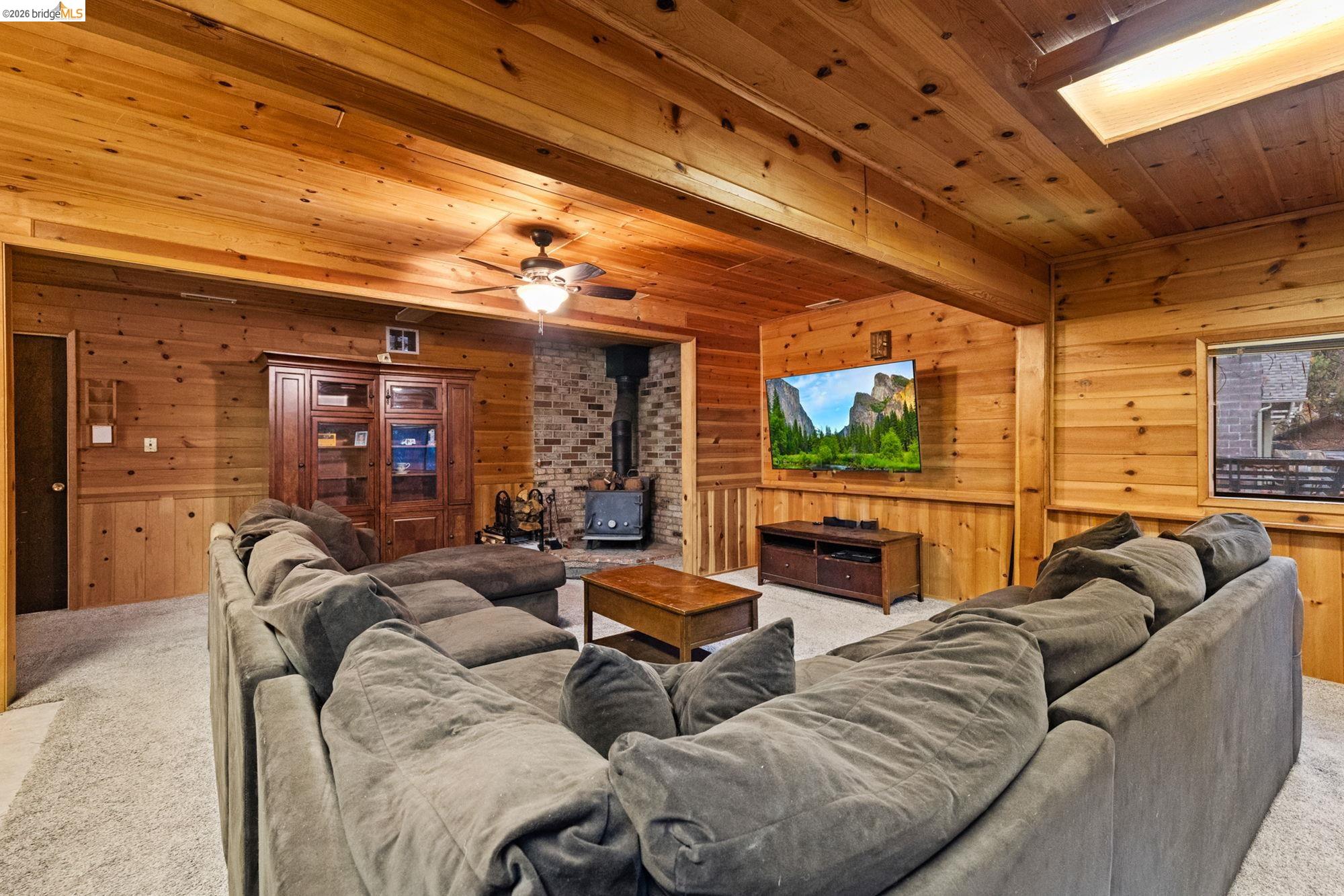 17851 Robin Road Twain Harte, CA 95383 - Photo 32 of 45 Carpeted living area featuring wooden walls, a wood stove, a ceiling fan, and a wooden ceiling with exposed beams