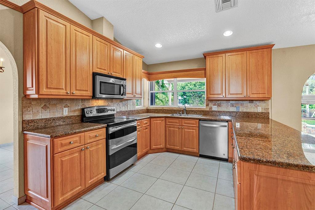 19571 Black Olive Lane Boca Raton, FL 33498 - Photo 11 of 61 a kitchen with stainless steel appliances granite countertop wooden cabinets a stove top oven a sink and dishwasher