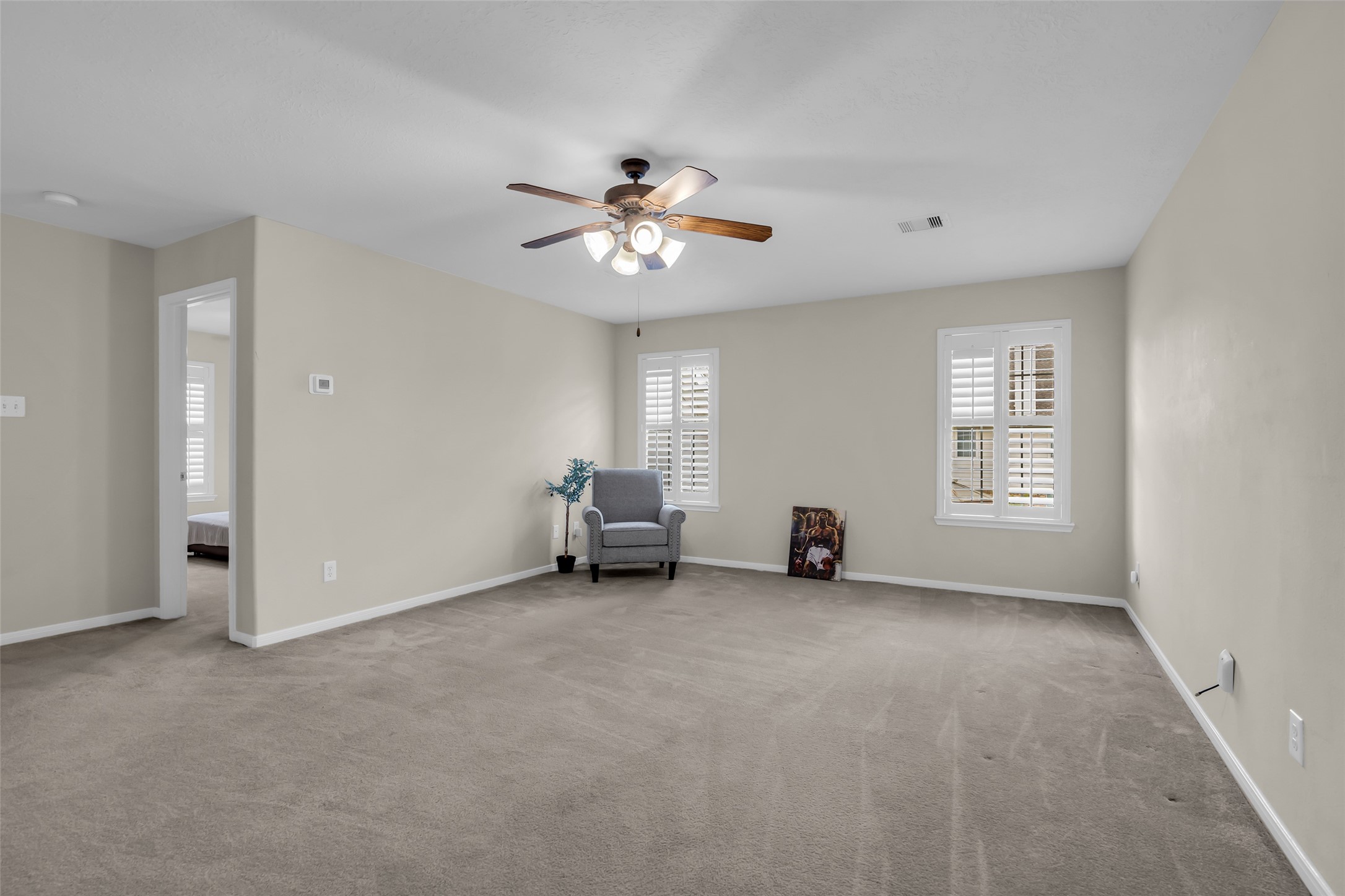 6807 Chapelfield Lane Houston, TX 77049 - Photo 32 of 42 Spacious room with neutral walls and carpet, featuring a ceiling fan and two windows with shutters for natural light. A cozy armchair sits in the corner, offering a comfortable reading nook.