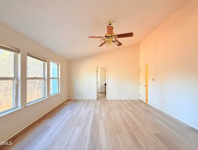 an empty room with wooden floor ceiling fan and windows