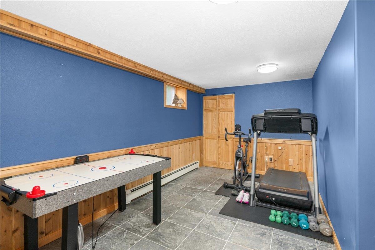 645 Stanley Road Two Harbors, MN 55616 - Photo 13 of 26 Exercise room featuring wood walls, a wainscoted wall, a baseboard radiator, and a textured ceiling