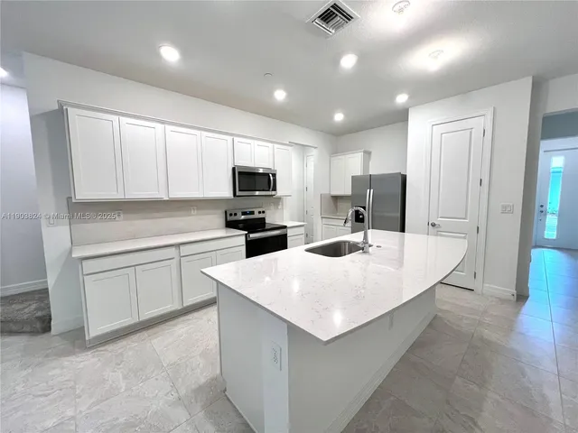 a large white kitchen with kitchen island a sink stainless steel appliances and cabinets
