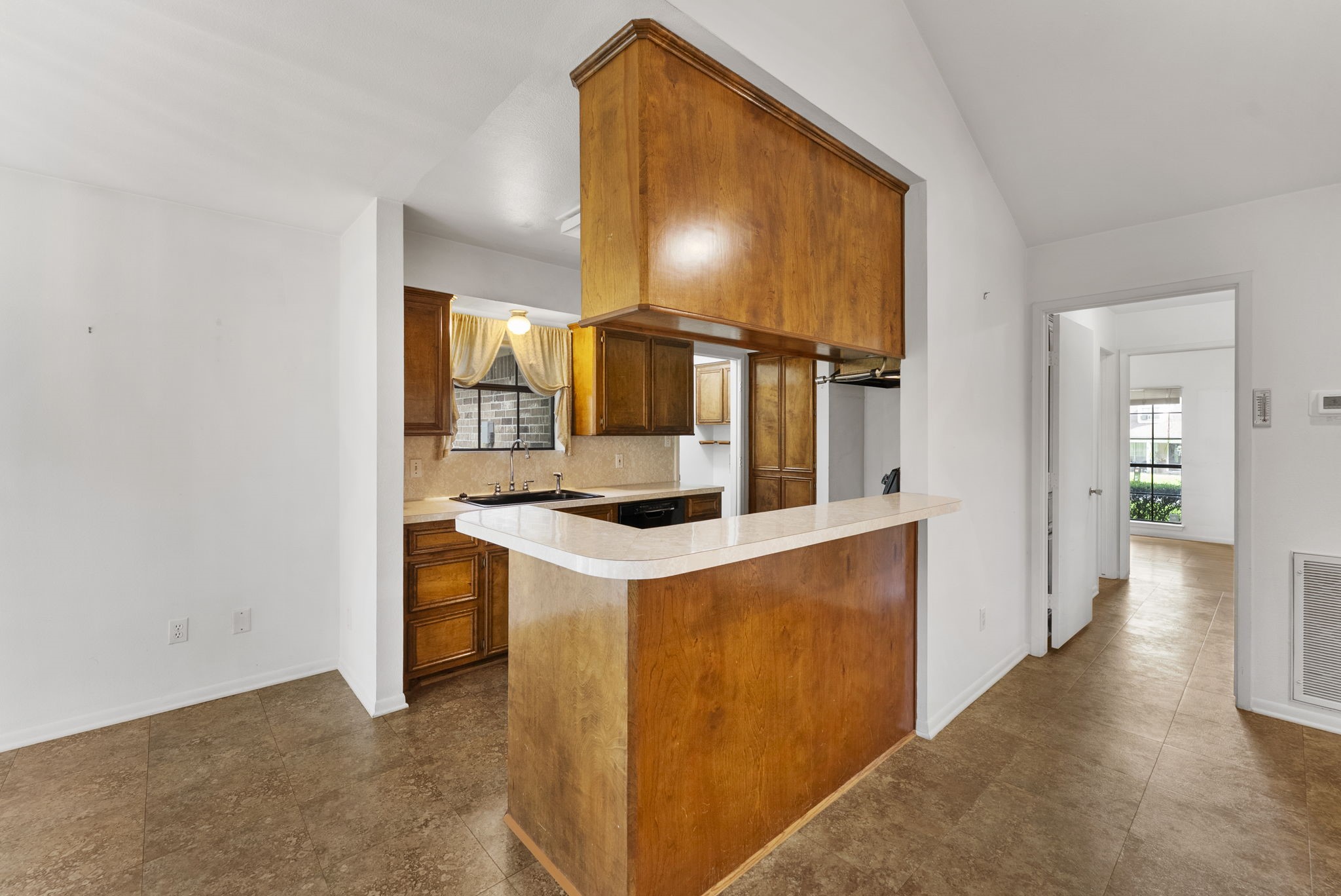 202 Sunset Boulevard Conroe, TX 77303 - Photo 14 of 50 This photo showcases a cozy kitchen area with warm wooden cabinetry and a breakfast bar. The space is open and leads into a bright adjoining room with large windows, offering a welcoming and functional layout.