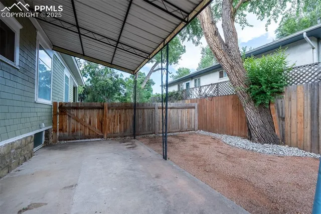 a view of a yard in front of a house with large tree and wooden fence