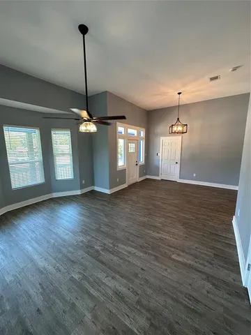 a view of an empty room with wooden floor and a ceiling fan