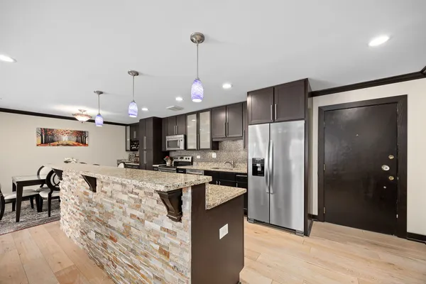 a kitchen with stainless steel appliances granite countertop a refrigerator a stove a sink a dining table and chairs with wooden floor