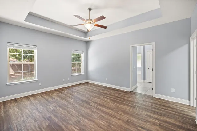 an empty room with wooden floor chandelier fan and windows