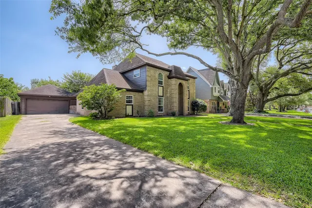 a view of a brick house with a big yard plants and large trees
