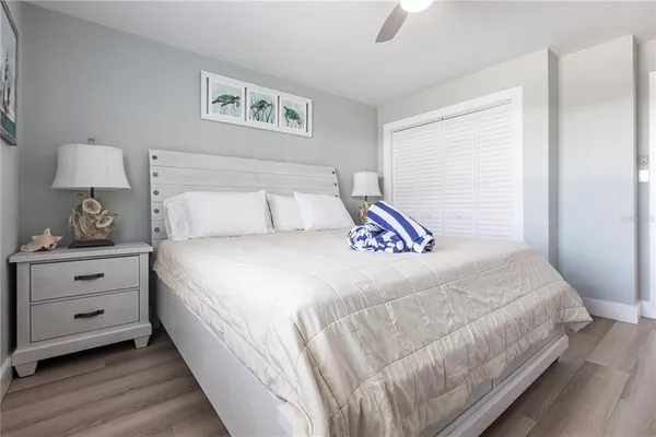 a bedroom with a bed and a lamp on dresser with wooden floor