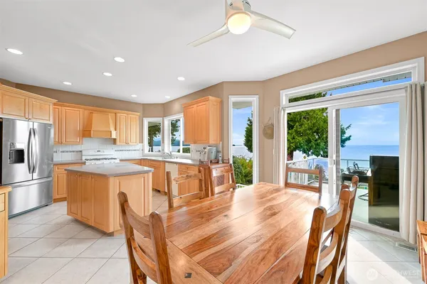 a kitchen with stainless steel appliances granite countertop a refrigerator a sink dishwasher a stove and a dining table with wooden floor