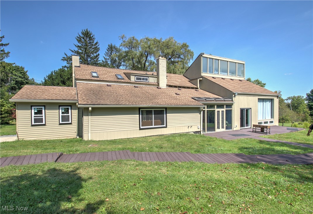 Rear view of house featuring a shingled roof, a chimney, a wooden deck, and a lawn