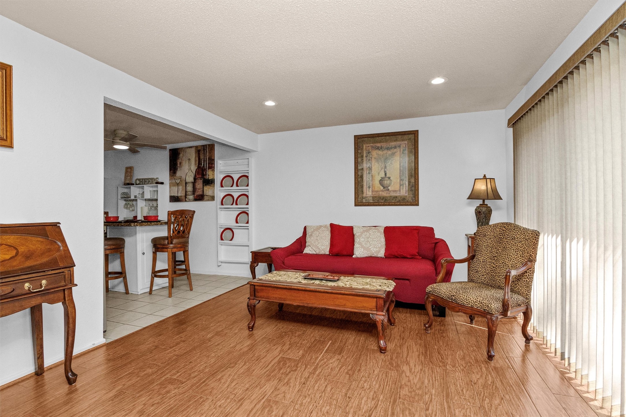 12900 Walden Road, Unit D 411 Montgomery, TX 77356 - Photo 8 of 18 This inviting living area boasts warm wood flooring, a vibrant red sofa with accent pillows, and a classic armchair, all bathed in natural light from a large window, seamlessly connecting to a cozy kitchen with a convenient breakfast bar.