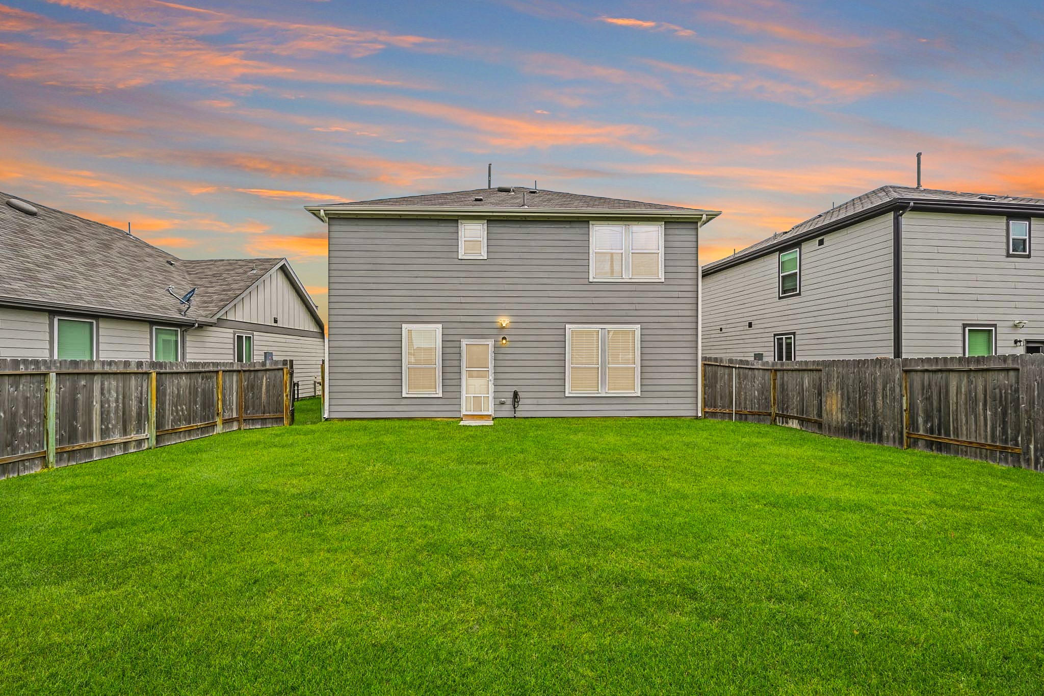 23427 Weir Box Road Hockley, TX 77447 - Photo 23 of 32 A straight-on look at the home’s back facade against a stunning sunset sky, highlighting the large windows that fill the interior with light and the generous width of the backyard lot.