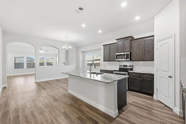 a kitchen with stainless steel appliances granite countertop a stove top oven a sink dishwasher a refrigerator and cabinets with wooden floor