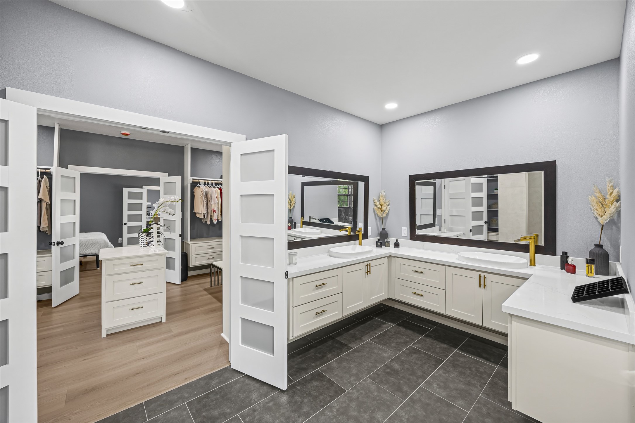 15080 Usher Lane Splendora, TX 77372 - Photo 30 of 44 This photo showcases a spacious bathroom with a modern design, featuring dual sinks, large mirrors, and ample cabinet storage. It seamlessly connects to a walk-in closet with stylish sliding doors, providing a functional and elegant space.