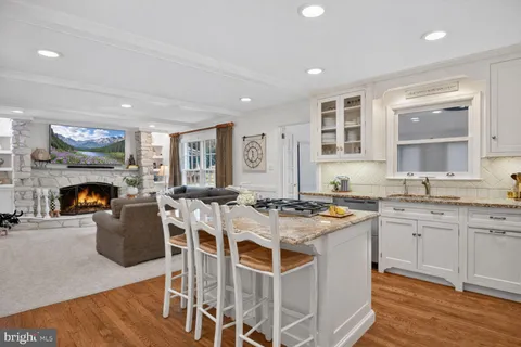 a kitchen with stainless steel appliances granite countertop a stove top oven a refrigerator a sink and white cabinets with wooden floor