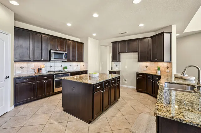 a kitchen with stainless steel appliances granite countertop a stove top oven a sink dishwasher a microwave oven and a refrigerator with wooden cabinets