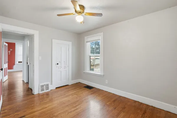 an empty room with wooden floor chandelier fan and windows