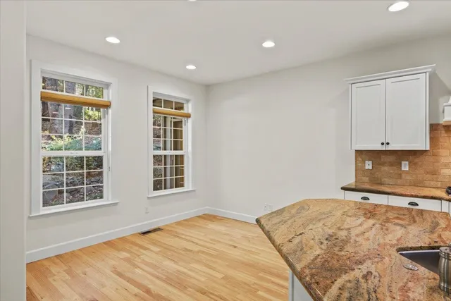 a large kitchen with stainless steel appliances granite countertop a stove a sink a refrigerator and white cabinets with wooden floor