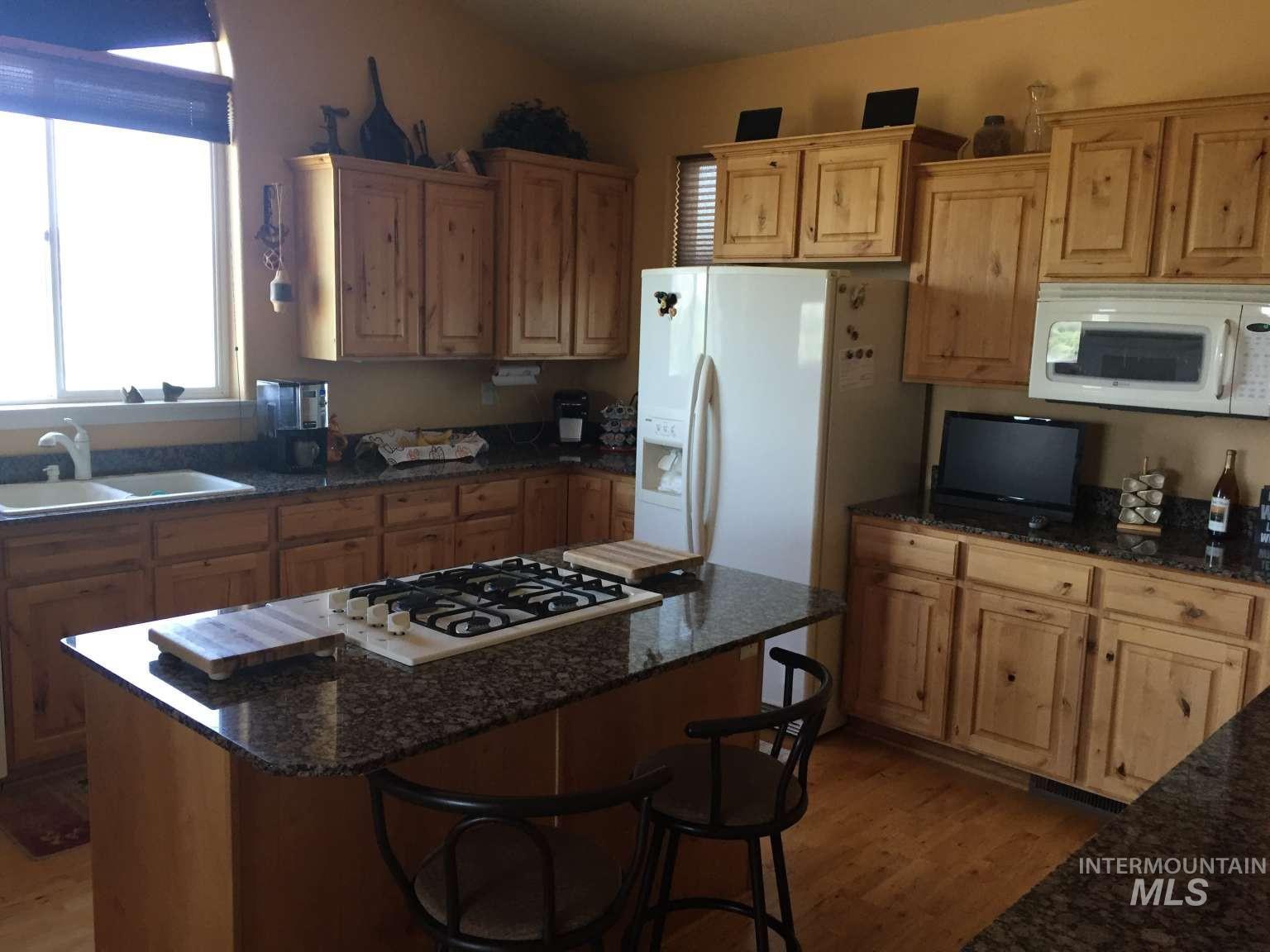 1422 River View Lane Buhl, ID 83316 - Photo 14 of 43 Kitchen featuring dark stone counters, white appliances, a kitchen island, wood finished floors, and a breakfast bar area