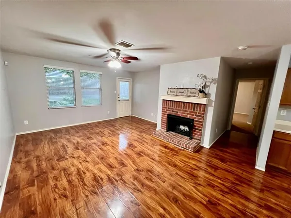 a view of an empty room with wooden floor fireplace and a window