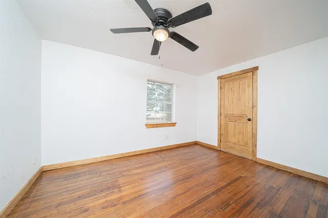 an empty room with wooden floor ceiling fan and windows