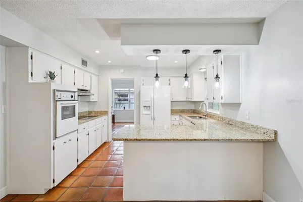 a large kitchen with granite countertop a sink and dishwasher a refrigerator a oven with white cabinets