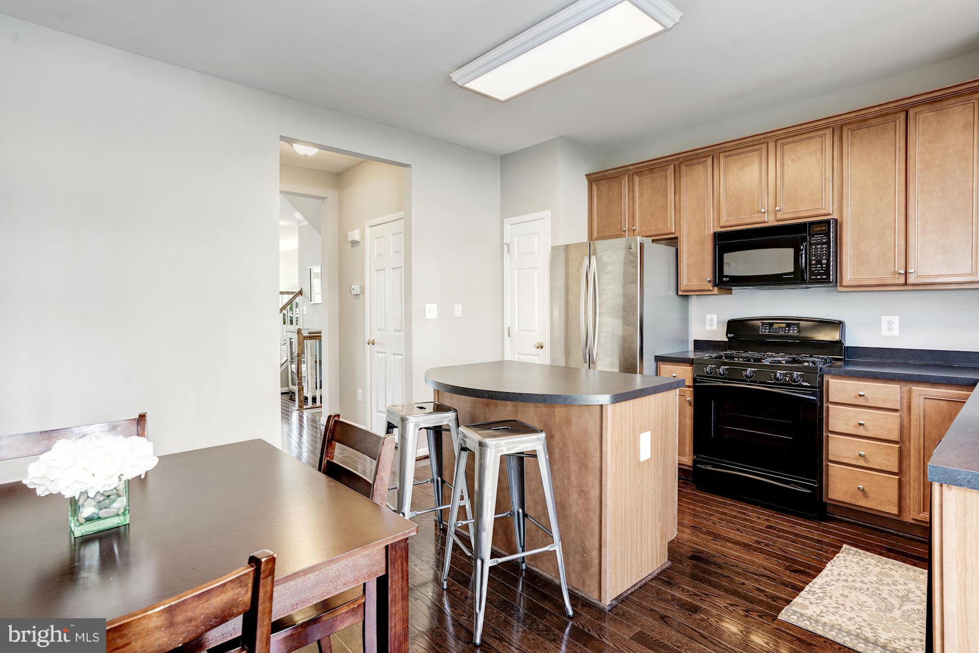 25013 Riding Center Drive Chantilly, VA 20152 - Photo 15 of 28 a kitchen with stainless steel appliances kitchen island granite countertop a stove a refrigerator a sink a dining table and chairs with wooden floor