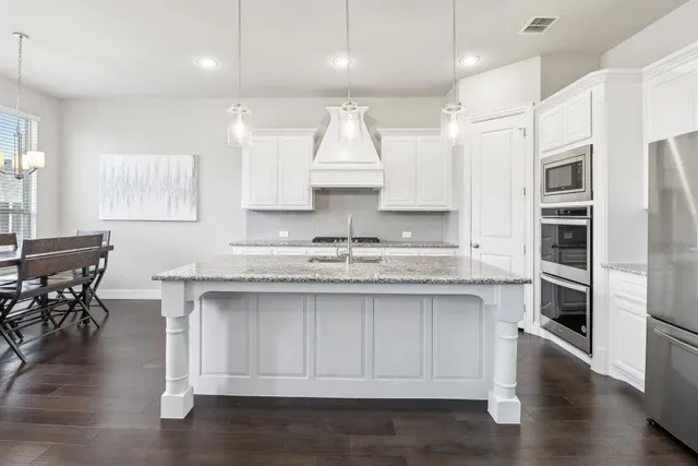 a kitchen with stainless steel appliances granite countertop a sink a stove a refrigerator and a dining table with wooden floor