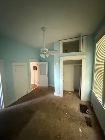 an empty room with chandelier fan and windows