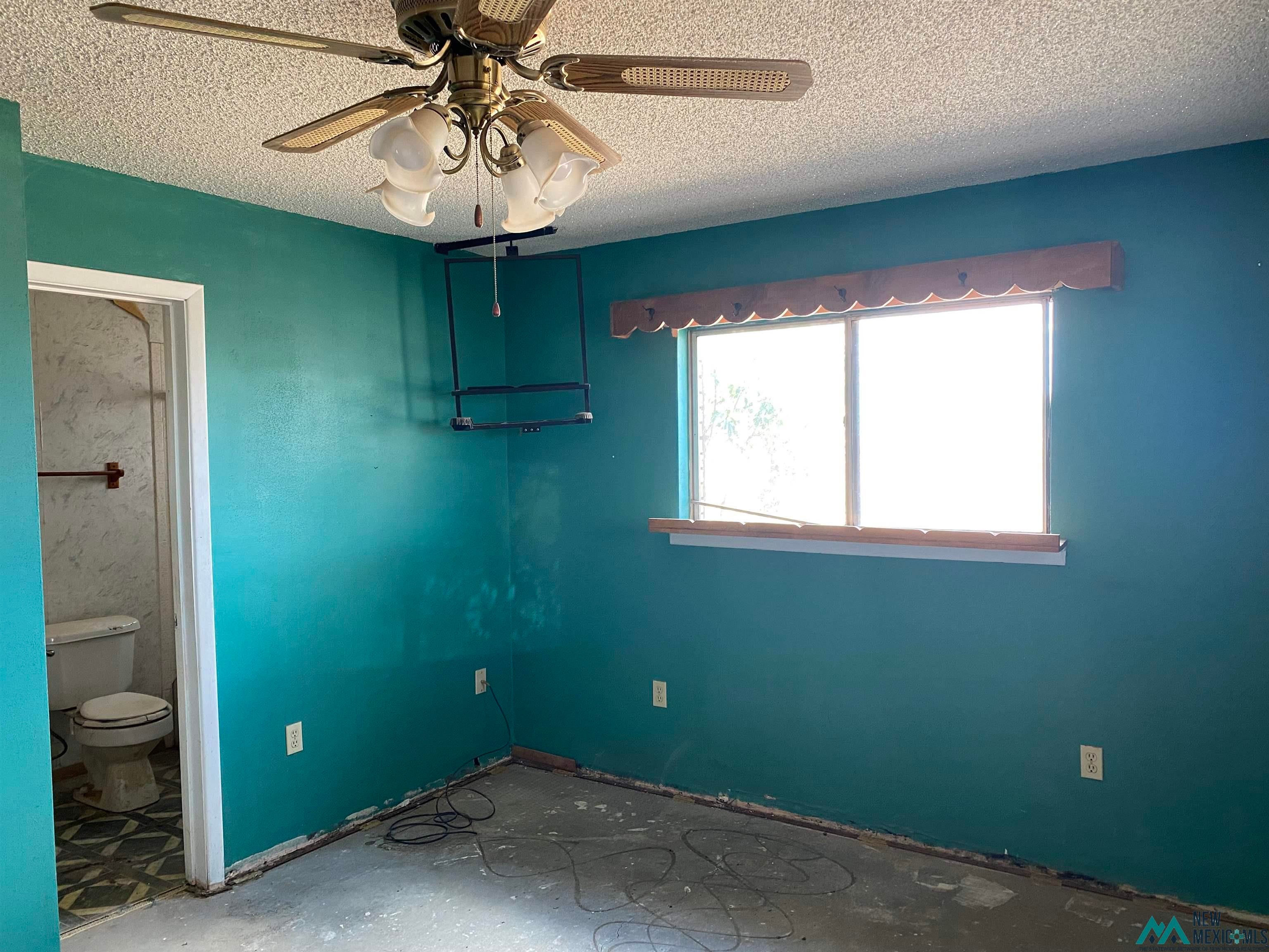 5985 Charolais Road Deming, NM 88030 - Photo 15 of 22 Room featuring a ceiling fan with integrated lighting, a window with a wood valance and sill, and an open doorway revealing a bathroom with a toilet and patterned floor tiles