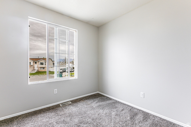 4239 West 5325th Street South Roy, UT 84067 - Photo 10 of 26 Room featuring a large window with grid pattern, light gray walls, and dark gray carpet flooring