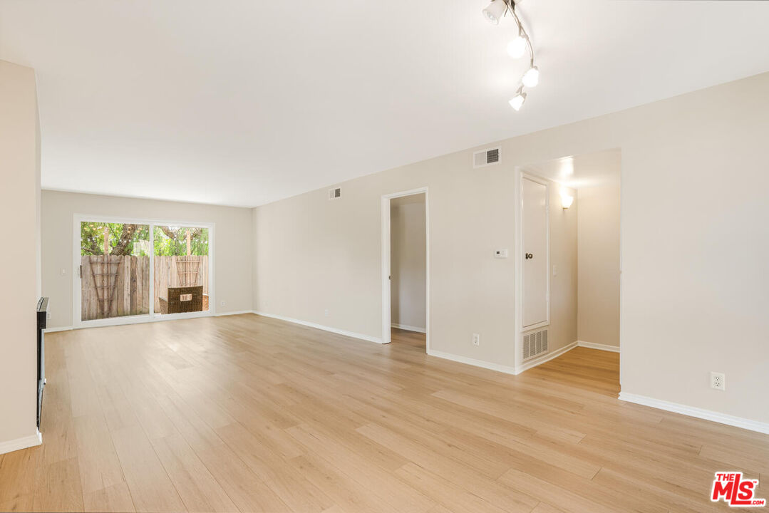 a view of an empty room with wooden floor and a window
