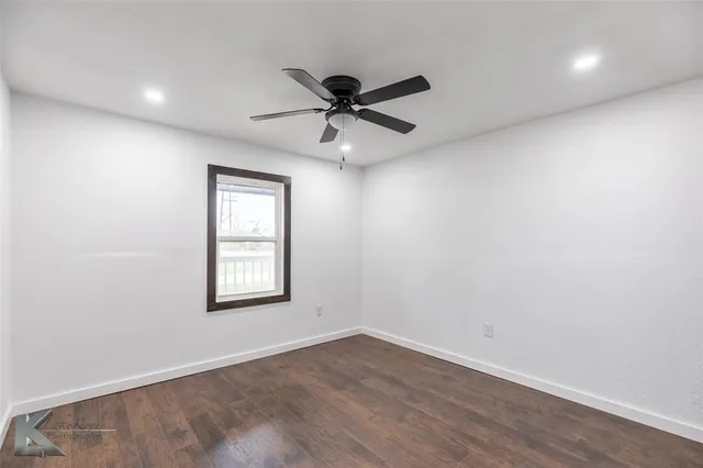 an empty room with wooden floor ceiling fan and windows