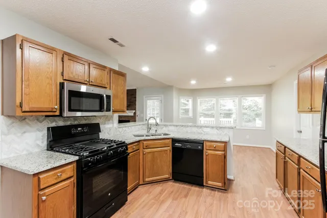 a kitchen with stainless steel appliances granite countertop a stove top oven a sink dishwasher a dining table and chairs with wooden floor