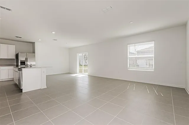 a view of an empty room with kitchen and window