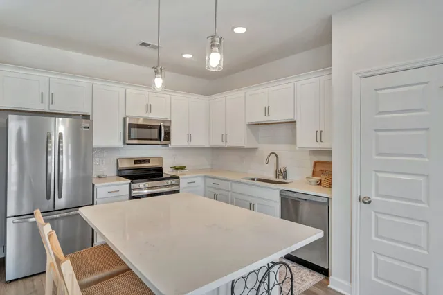 a kitchen with stainless steel appliances a stove a sink a refrigerator white cabinets and wooden floor