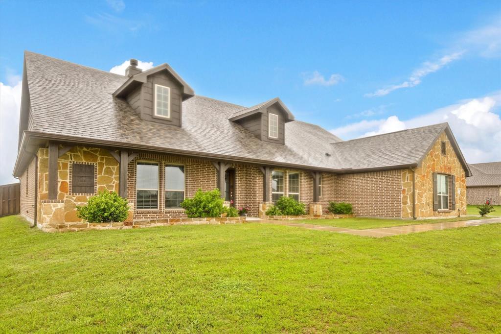 New england style home with stone siding, roof with shingles, and a front lawn