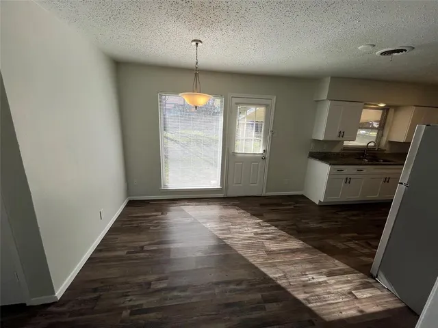 an empty room with wooden floor kitchen view and windows