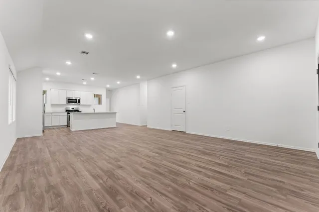 a view of an empty room with wooden floor and a kitchen