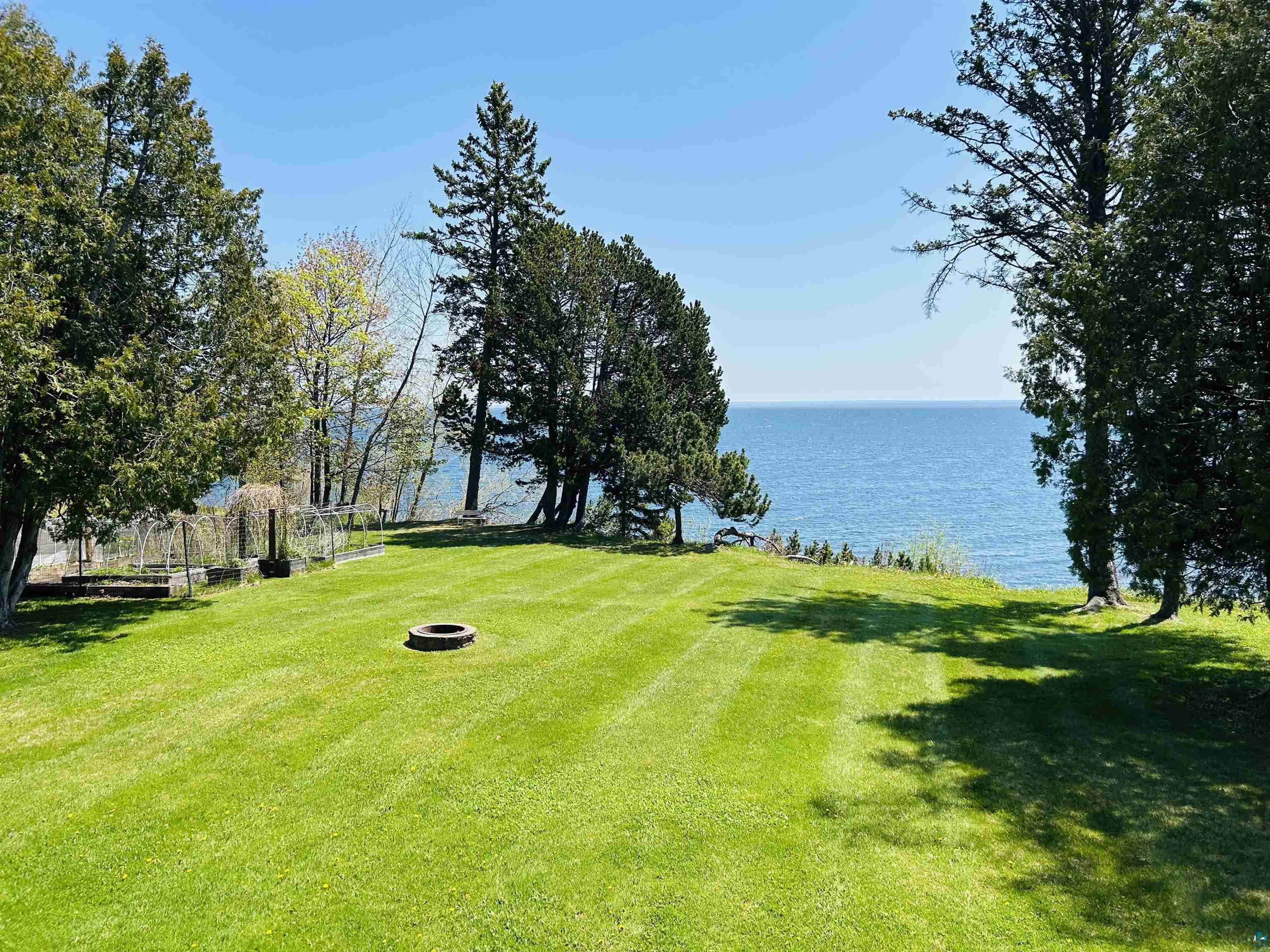 5090 London Road, Unit 1 Duluth, MN 55804 - Photo 40 of 54 Expansive grassy lawn with a stone fire pit, bordered by mature trees and evergreen foliage