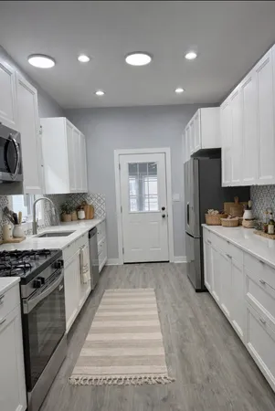 a kitchen with granite countertop a stove top oven a sink dishwasher a refrigerator and white cabinets with wooden floor