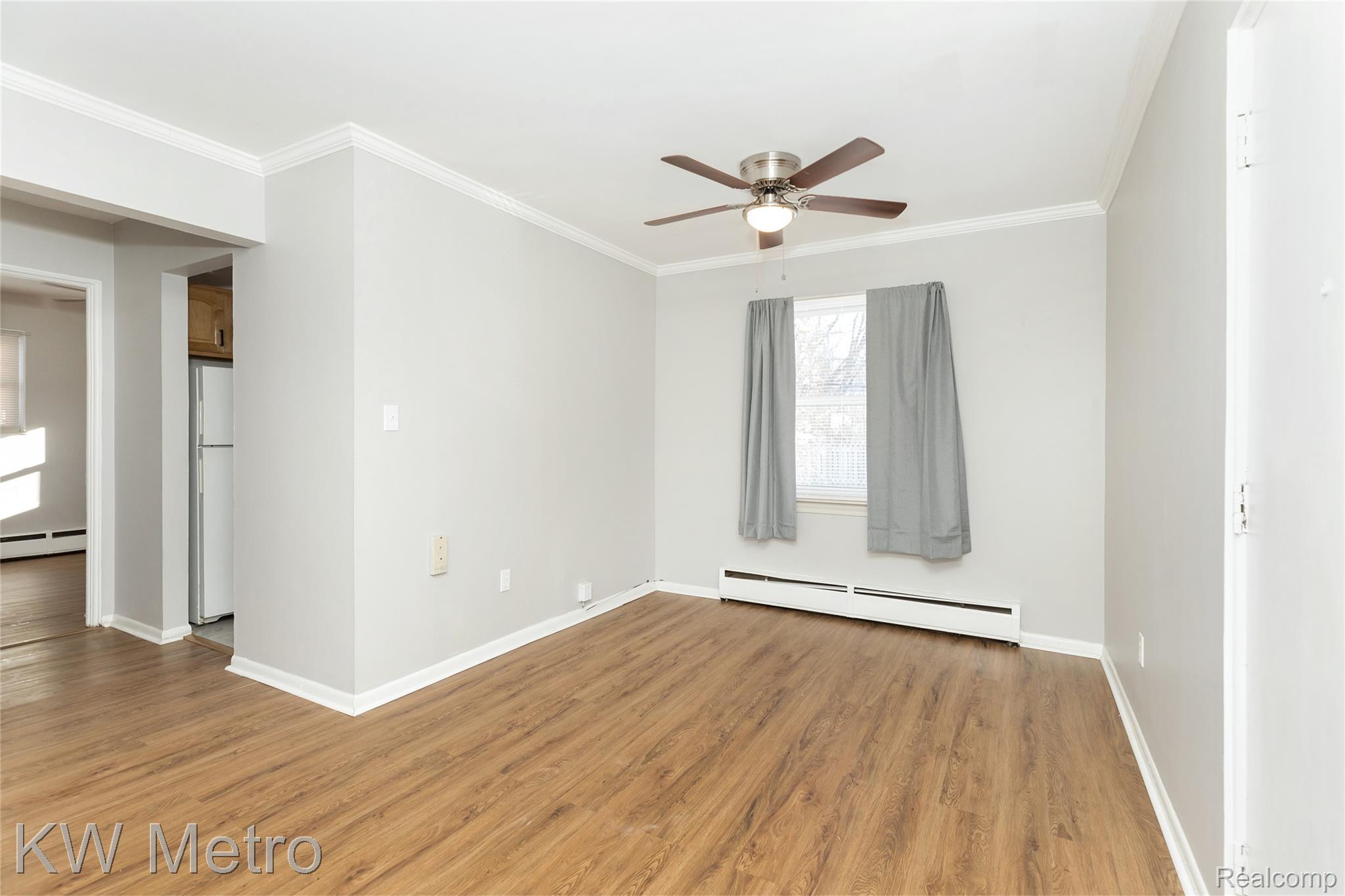 2817 West 13 Mile Road Royal Oak, MI 48073 - Photo 7 of 21 Unfurnished room featuring baseboard heating, light wood finished floors, a ceiling fan, and crown molding