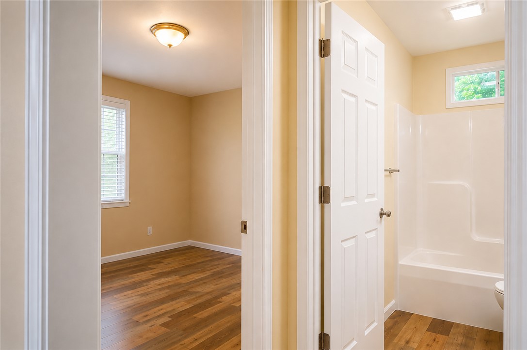 605 Hampton Street Iva, SC 29655 - Photo 10 of 16 A well-maintained full bathroom featuring a shower-tub combo and a bright bedroom with warm wooden flooring.