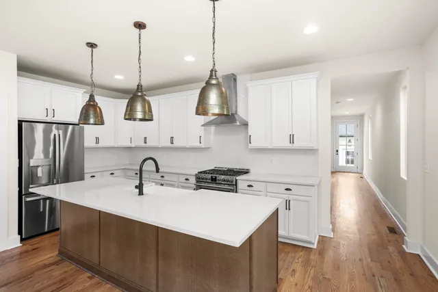 a kitchen with stainless steel appliances a sink a stove a refrigerator and white cabinets with wooden floor