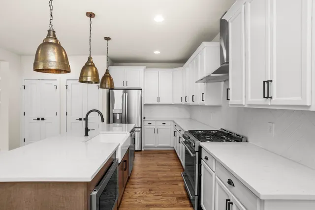 a kitchen with stainless steel appliances a sink a stove a refrigerator and white cabinets