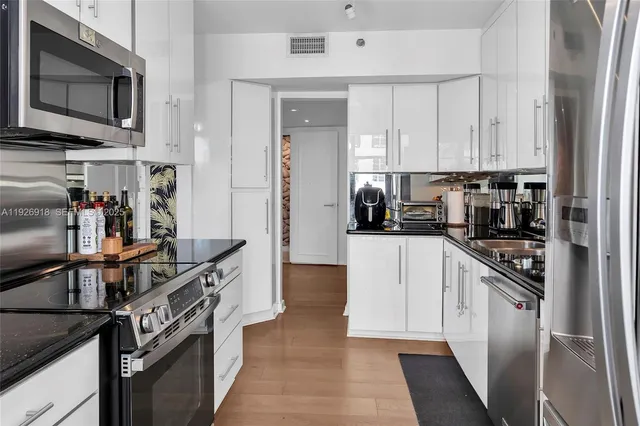 a kitchen with stainless steel appliances a stove top oven a sink a refrigerator white cabinets and wooden floor