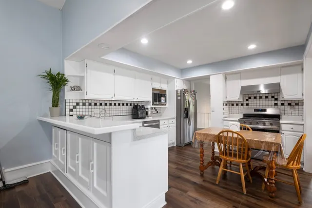 a kitchen with stainless steel appliances kitchen island granite countertop a refrigerator a stove a sink dishwasher and white cabinets with wooden floor