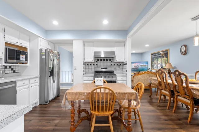 a kitchen with stainless steel appliances kitchen island granite countertop a refrigerator a stove a microwave oven a dining table and chairs with wooden floor