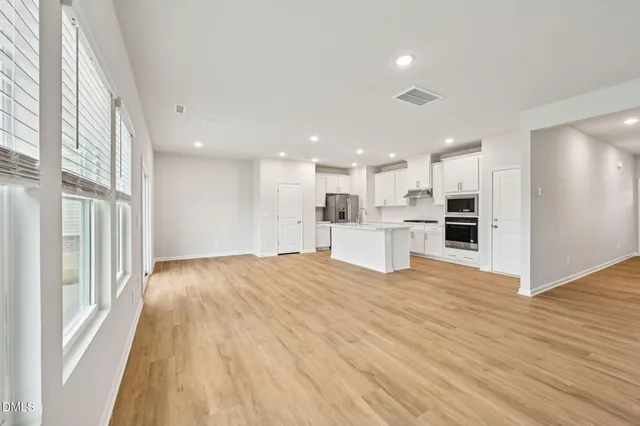 a view of empty room with wooden floor and kitchen view